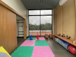 Sala ampla com piso de tapetes coloridos e grande janela com vista para um campo esportivo.