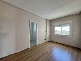 Interior de uma sala com piso de madeira e janela com vista para a cidade.