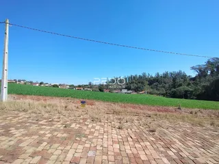 Vista externa de um terreno com piso de tijolos e campo aberto sob um céu azul.