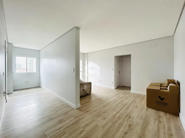 Interior de uma sala com piso de madeira clara e paredes brancas.