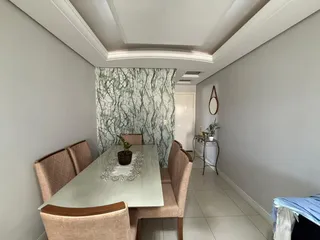 Uma sala de jantar longa com mesa e cadeiras estofadas em um ambiente claro.