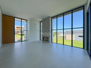 Vista interna de uma sala ampla com grandes janelas que dão para um jardim.