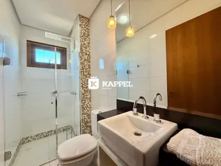 Banheiro com box de vidro, pia e revestimento de azulejos.