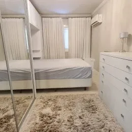 Quarto com cama de casal e cortinas brancas.