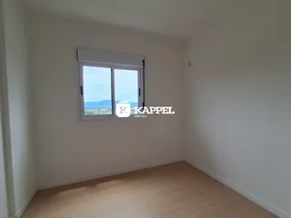 Foto de um cômodo interno com paredes brancas e piso de madeira, mostrando uma janela com vista.