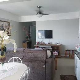Foto interna de uma sala de estar com sofá e televisão montada na parede.