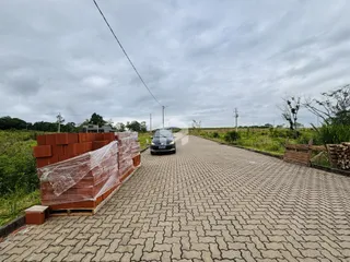 Uma estrada pavimentada com blocos de concreto e uma cerca de tijolos são visíveis na propriedade.