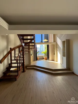Vista de um corredor com escadaria de madeira em um imóvel.