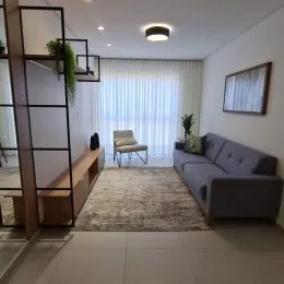 Sala de estar iluminada com cortinas brancas e um sofá cinza.