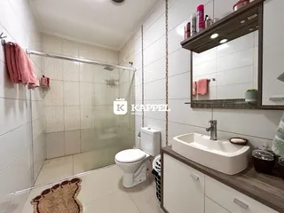 Banheiro com box de vidro, vaso sanitário e bancada de pia.