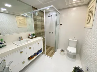 Foto de um banheiro com bancada branca e box de vidro transparente.