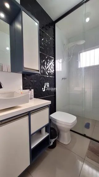 Interior de um banheiro com revestimento escuro e box de vidro.