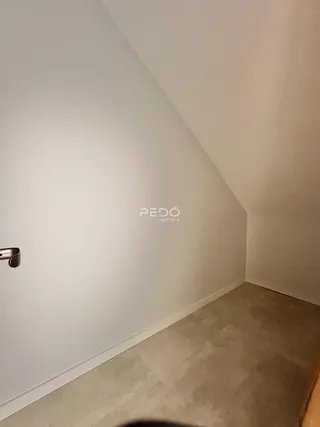 Vista de um canto interno de uma sala com paredes brancas.