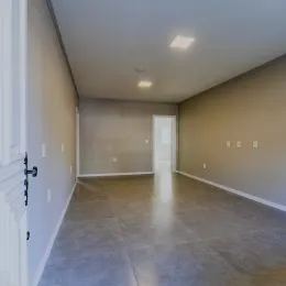 Uma foto de um corredor interno com paredes claras e piso cinza.