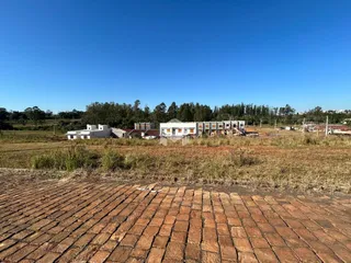 Vista externa de uma propriedade com terreno e edificações ao fundo.