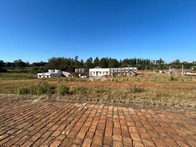 Vista externa de uma propriedade com terreno e edificações ao fundo.