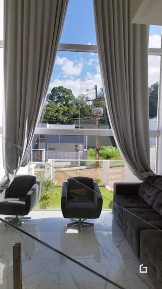 Vista interna de uma sala com grandes janelas e cortinas claras.