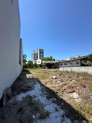 Vista externa de um terreno com vegetação e entulho ao lado de um prédio.