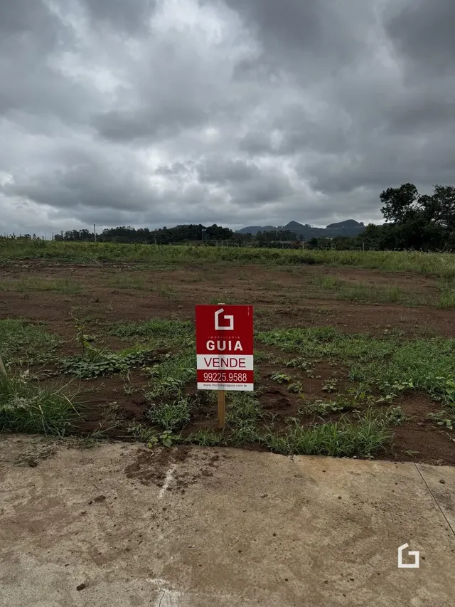 Vista externa de um terreno aberto com vegetação e uma placa no meio.