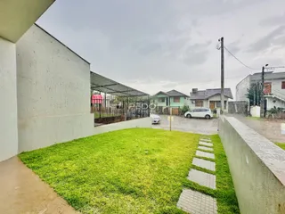Vista externa de um quintal gramado com cerca e casas ao fundo.