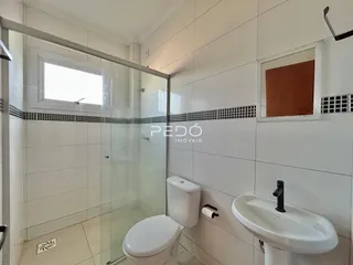 Banheiro com box de vidro, vaso sanitário e pia brancos.