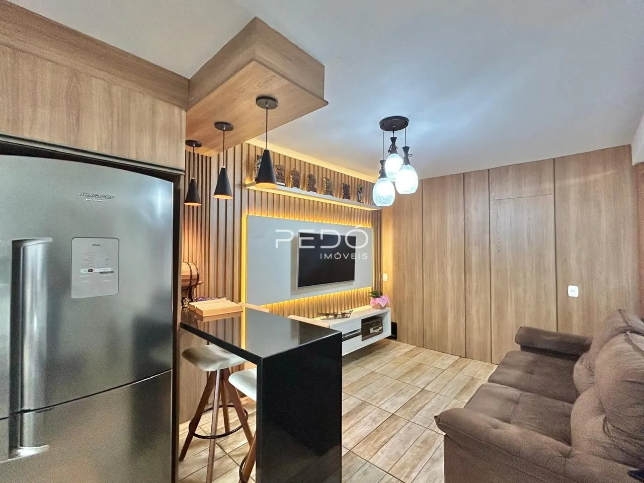 Interior de uma sala de estar com acabamentos em madeira e cozinha moderna.