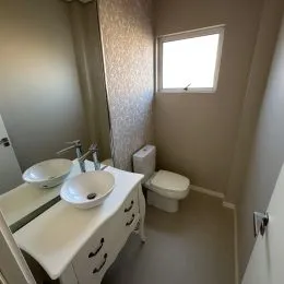 Foto de um banheiro com bancada branca e gabinete.
