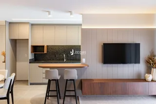 Interior de uma cozinha e sala de estar moderna com ilha e televisão.