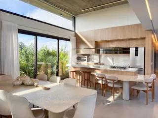 Ambiente moderno de sala de jantar e cozinha com vista para a vegetação externa.