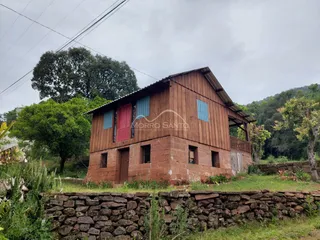 Fachada de uma casa de tijolos vermelhos em uma área rural com vegetação ao redor.