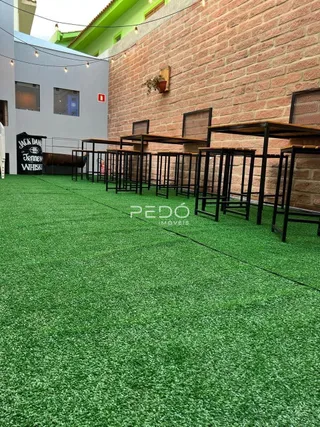 Área externa com piso de grama sintética e mesas de jantar.