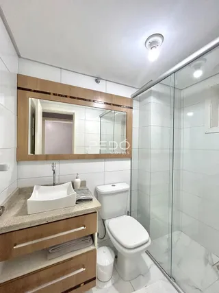 Banheiro com box de vidro e louças brancas.