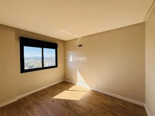 Vista interna de uma sala com piso de madeira e grande janela.