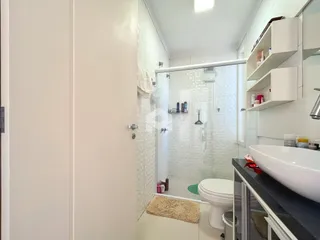Interior de um banheiro com box de vidro e revestimento branco.