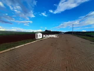 Vista externa de uma propriedade com pátio pavimentado e campo aberto ao fundo.