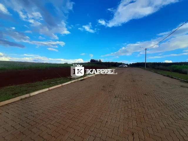 Vista externa de uma propriedade com pátio pavimentado e campo aberto ao fundo.