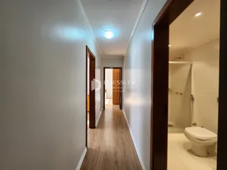 Corredor interno de uma residência com piso de madeira clara.