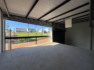 Vista externa de uma estrutura com telhado metálico e vista para um campo aberto.