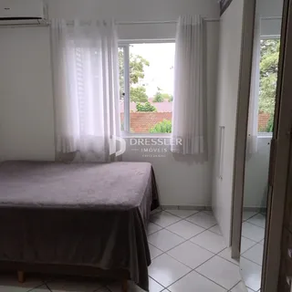 Quarto com cama e janela com cortinas brancas.