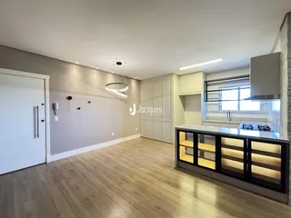 Ambiente interno de uma sala de estar com piso de madeira clara e cozinha moderna.