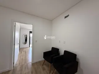 Interior de uma sala com piso de madeira e duas poltronas pretas.