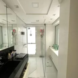 Interior de um banheiro com box de vidro e revestimento branco.