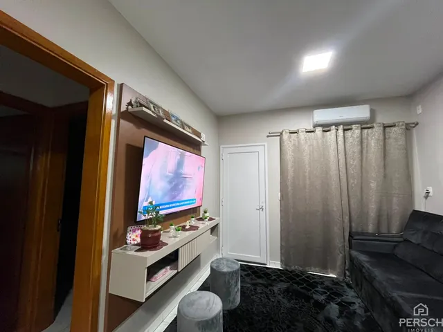 Sala de estar com televisão montada na parede e cortinas claras.