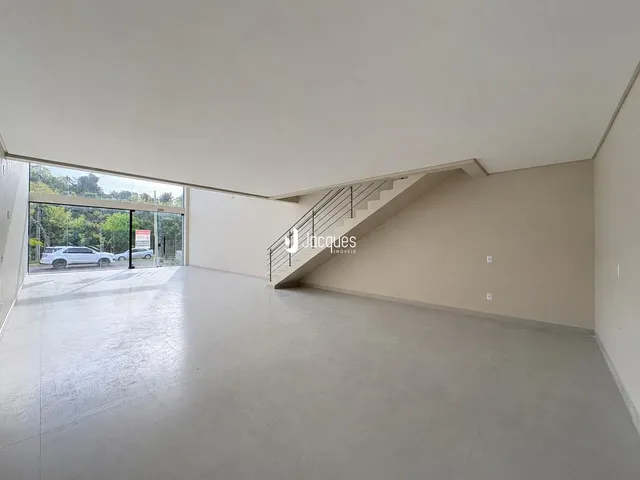 Vista interna de um espaço amplo com paredes brancas e acesso ao exterior.