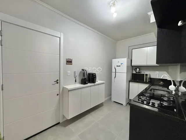 Vista interna de uma cozinha moderna com armários brancos e piso claro.