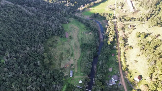 Vista aérea da propriedade mostrando uma área verde com um rio e estrada rural.