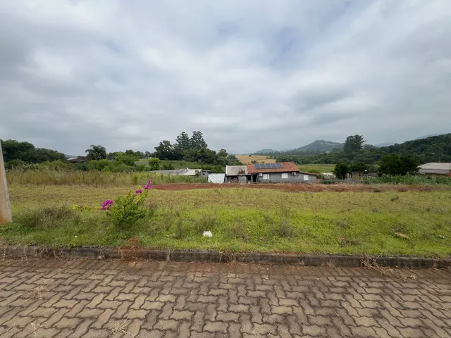 Vista externa de uma propriedade rural com vegetação e estruturas ao fundo.