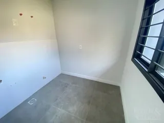 Vista interna de um corredor com paredes brancas e piso de concreto claro.
