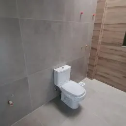 Foto de um banheiro mostrando um vaso sanitário branco em um ambiente com revestimento de parede cinza claro.