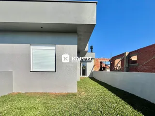 A foto exibe a fachada moderna de uma residência com jardim gramado sob um céu azul claro.